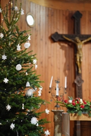 Ein mit weißem Schmuck geschmückter Tannenbaum steht in einer Kirche. Im Hintergrund ein Kreuz.