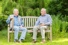 Symbolbild: Zwei Männr sitzen auf einer Bank und unterhalten sich.